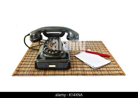 Téléphone vintage sur tapis en rotin avec stylo rouge et le bloc-notes avec copyspace isolé sur fond blanc Banque D'Images