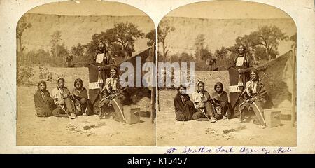 Carte stéréographique montrant un groupe de personnes Sioux, trois femmes assises sur le sol, un homme assis sur un fort fumer une pipe, et un homme debout, manuscrite au bas de photo est à queue tachetée, Nebraska, 1865 de l'Agence. Banque D'Images