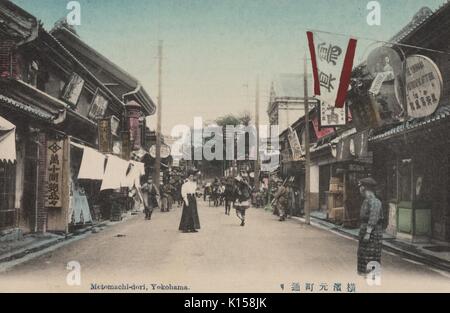 Une carte postale créée à partir d'une photographie teinté, les gens peuvent être vu sur pied et d'être entraînée dans des charrettes, la rue est bordée de commerces, Motomachi-dori, Yokohama, Japon, 1911. À partir de la Bibliothèque publique de New York. Banque D'Images