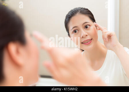 Photo gros plan de sweet pretty smiling boy crème visage sur le doigt à miroir à joues soins dans la salle de bains avec la réflexion de l'image. Banque D'Images