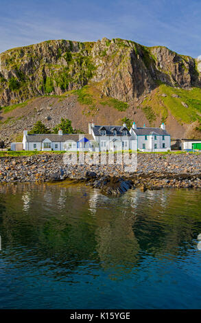 Superbe vue sur le village d'Easdale Ellenabeich /, Seil Island, en Ecosse, avec blanc cottages à la base de la falaise rocheuse reflète dans les eaux calmes de l'océan Banque D'Images