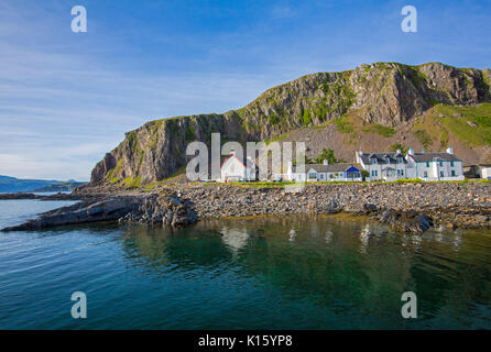 Superbe vue sur le village d'Easdale Ellenabeich /, Seil Island, en Ecosse, avec blanc cottages à la base de la falaise rocheuse reflète dans les eaux calmes de l'océan Banque D'Images