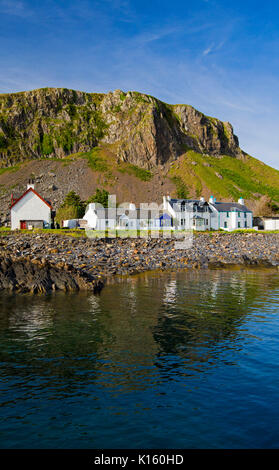 Superbe vue sur le village d'Easdale Ellenabeich /, Seil Island, en Ecosse, avec blanc cottages à la base de la falaise rocheuse reflète dans les eaux calmes de l'océan Banque D'Images