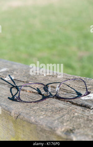 Perdu paire de lunettes cassées sur bois banc de parc Banque D'Images