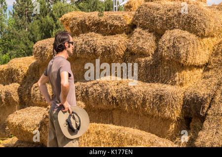 Beau gars avec hat debout avec les mains sur sa taille près de bottes de paille. Banque D'Images