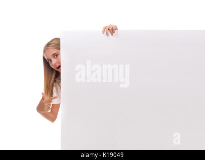 Surpris teen girl est popping out du côté de white blank banner et de pointage de l'office au fond blanc Banque D'Images