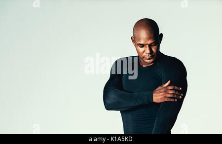 Portrait de beaux jeunes gens en t-shirt de sport sur fond gris. Modèle masculin africain portant des T-shirt de compression touchant ses biceps. Banque D'Images