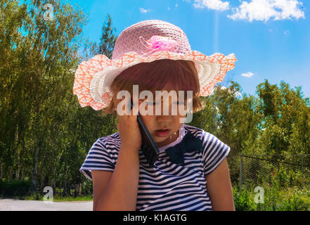 Kid avec smartphone avec un visage sérieux. little baby girl téléphone cellulaire de parler à sa maman, papa famille le vert des arbres à l'extérieur de l'été l'arrière-plan. Les enfants Banque D'Images