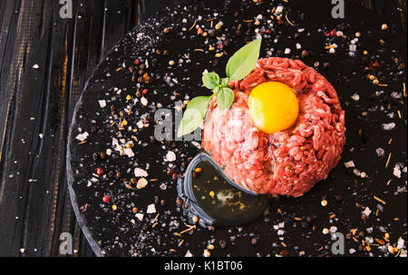 Steak tartare de matières de la viande hachée avec du sel et d'épices, sur un fond noir, selective focus, de l'espace pour le texte Banque D'Images