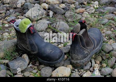 Une sale paire de bottes de travail redback enfant, abandonné sur le sol rocheux. Banque D'Images