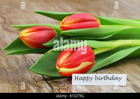 Joyeux anniversaire carte avec trois tulipes colorées sur la surface en bois Banque D'Images