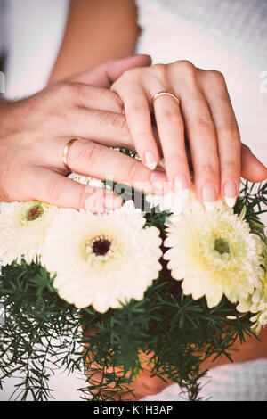 Mains de jeunes mariés avec joints toriques sur le bouquet de mariage inhabituel. Banque D'Images