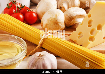 Ingrédients pâtes. Les tomates cerise, les pâtes spaghetti, l'ail, le fromage et les champignons sur une table de cuisine Banque D'Images