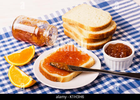 Pot de confiture d'orange avec du pain sur la nappe bleue à carreaux, gros plan Banque D'Images