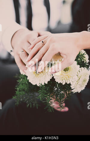 Mains de jeunes mariés avec joints toriques sur le bouquet de mariage inhabituel. Banque D'Images