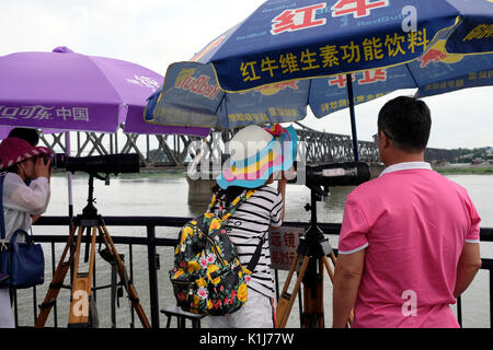 Dandong, province de Liaoning, Chine - 29 juillet 2017 : les touristes à la recherche au moyen d'un télescope à partir de la rivière Yalu pont cassé à Sinuiju en Corée du Nord. Banque D'Images