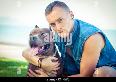 L'homme et le chien bull-terrier américain de mine de détente à l'initiative Faire place au parc et s'étreindre Banque D'Images