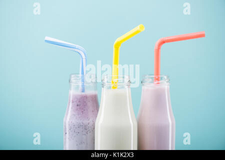 Vue rapprochée de délicieux milk-shakes de fruits en bouteilles de verre avec des pailles à isolé sur blue Banque D'Images