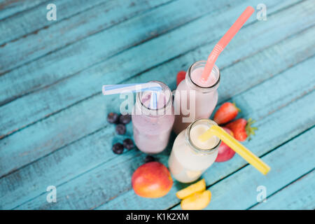 Vue rapprochée de délicieux milk-shakes en bouteilles de verre avec des pailles à boire et des fruits sur la table en bois Banque D'Images