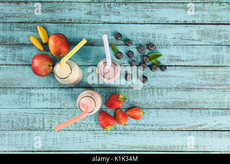 Vue de dessus de milkshakes en bouteilles de verre avec des baies et fruits sur une table en bois Banque D'Images