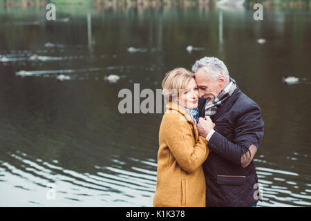 Close-up portrait of beautiful mature couple debout et tenant les mains près de lake in autumn park Banque D'Images