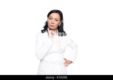 De graves brunette woman in white coat debout avec la main sur la taille et looking at camera Banque D'Images