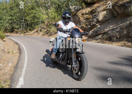 Vue de côté de l'homme assis sur la moto custom parqué sur route dans les montagnes. Banque D'Images