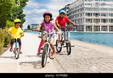 Portrait of African 6-7 ans girl riding bicycle avec ses amis sur un remblai de la rivière en été Banque D'Images