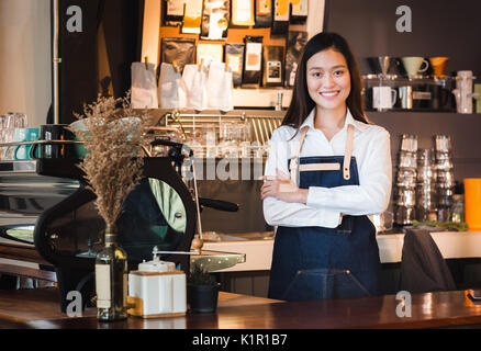 Asian female barista de porter un tablier jean croisa les bras au comptoir bar avec smile face,cafe service concept,propriétaire démarrage d'entreprise. Banque D'Images