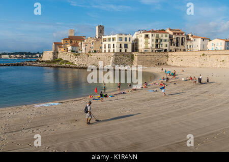 Un homme utilise un détecteur de métal sur une plage avec vue sur Antibes, Côte d'Azur, France Banque D'Images