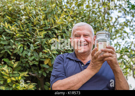 Old man smiling while holding un pot plein de billets sur la nature de fond vert Banque D'Images