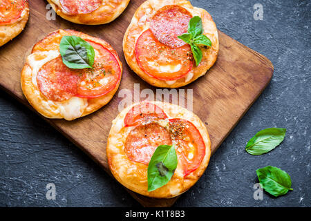 Mini Pizza - des mini pizzas pepperoni, fromage, tomates et basilic sur fond noir en noir rustique. Banque D'Images