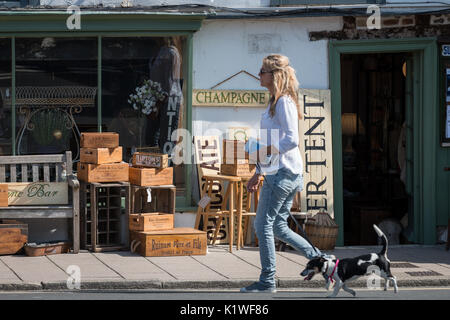 Une femme marche un chien passé les caisses en bois et d'autres articles en vente à l'extérieur d'une boutique d'antiquités à Arundel, West Sussex, Angleterre. Banque D'Images