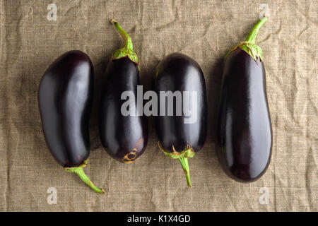 Quatre aubergines noirs mûrs sur toile tissu. Vue supérieure rustique Banque D'Images