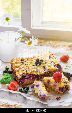 Le cassis, fraise et cottage gâteau crumble avec des feuilles vertes sur du papier sulfurisé et fond rustique Banque D'Images