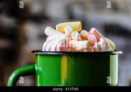 Le mug émaillé vert est rempli d'une guimauve multicolore sur fond intérieur floue close-up Banque D'Images