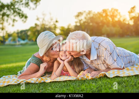 Les grands-parents kissing heureux petite-fille. Sourire de l'enfant à l'extérieur. En prenant soin de leurs petits-enfants. Banque D'Images