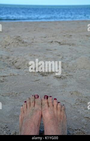 Pieds de sable avec des ongles rouges sur la plage avec la mer en arrière-plan flou Banque D'Images