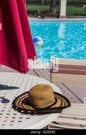L'été de womans hat sur une table au bord d'une piscine communautaire avec un flottant dans l'beachball clair comme de l'eau sur une chaude journée d'été en Californie Banque D'Images