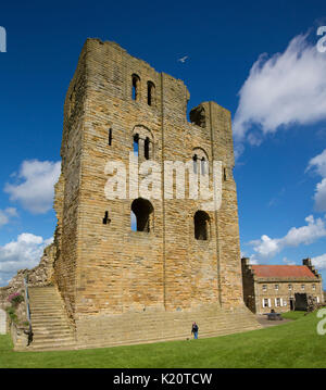 Ruines imposantes de tower / donjon de château anglais du 12ème siècle historique avec l'homme à sa structure de base dérisoire par s'élevant dans le ciel bleu à Scarborough Banque D'Images