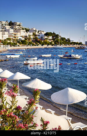 Parasols et chaises longues blanc près de lagon avec des bateaux sur la plage à Bodrum, Turquie Banque D'Images