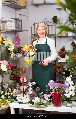 Friendly smiling mature female florist avec clippers la préparation de fleurs à vendre Banque D'Images