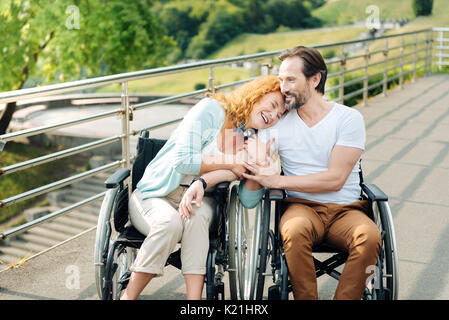 Cheerful senior woman embracing son tendre mari wheelchaired Banque D'Images