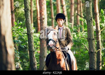 Adolescente dans l'usure formelle à cheval en forêt. Banque D'Images