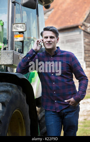 Farmer prochain au tracteur Talking On Mobile Phone Banque D'Images