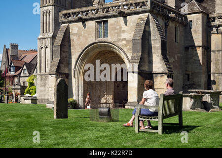 Un couple de visiteurs assis sur un banc, sur une journée ensoleillée dans le cimetière du 7ème siècle l'abbaye de Malmesbury, un jour ensoleillé, dans le Wiltshire, uk Banque D'Images