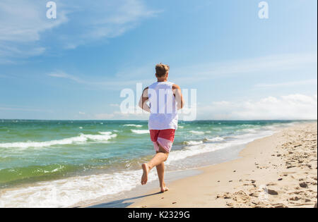 Heureux homme qui court le long de la plage d'été Banque D'Images