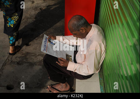 19.10.2013, Yangon, République de l'Union du Myanmar, de l'Asie - Un homme est vu assis sur le trottoir de la lecture d'un journal. Banque D'Images