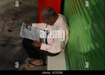 19.10.2013, Yangon, République de l'Union du Myanmar, de l'Asie - Un homme est vu assis sur le trottoir de la lecture d'un journal. Banque D'Images