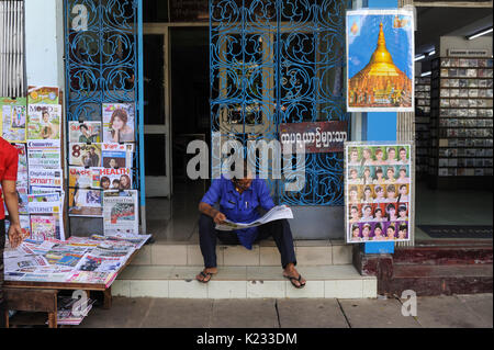 01.10.2013, Yangon, République de l'Union du Myanmar, de l'Asie - Un homme est vu assis sur le trottoir de la lecture d'un journal. Banque D'Images